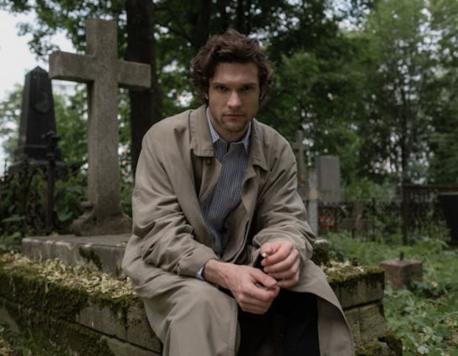 A Man in a Trench Coat Sitting on a Grave