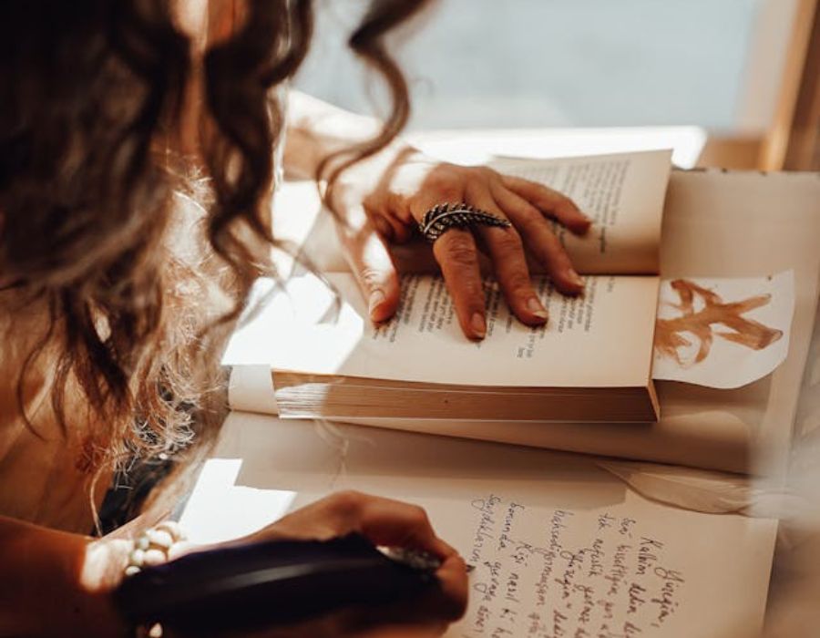 a woman writing with reference to a book