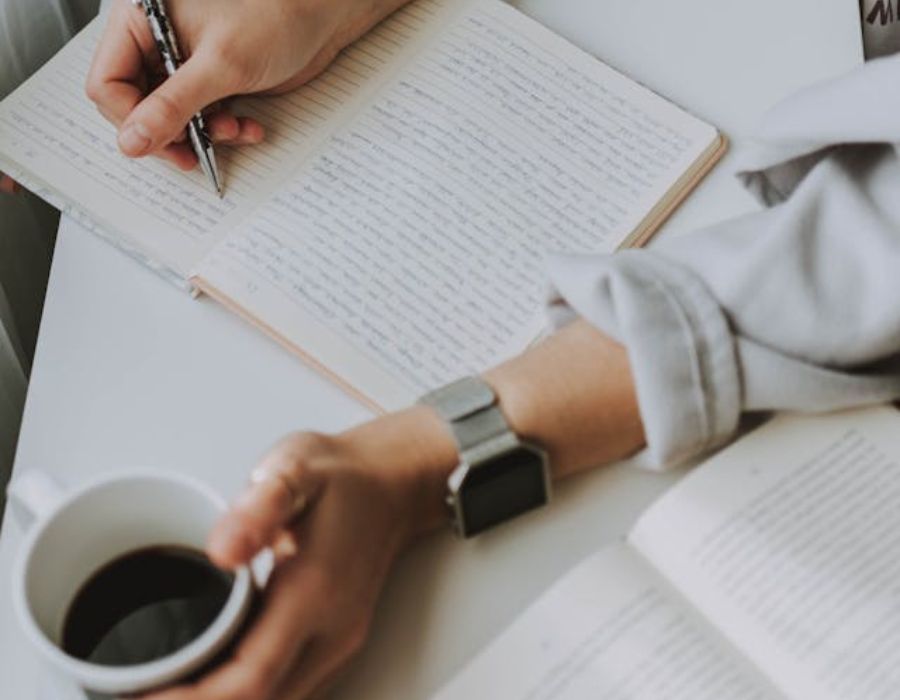 a woman writing an eulogy while holding a mag of coffe
